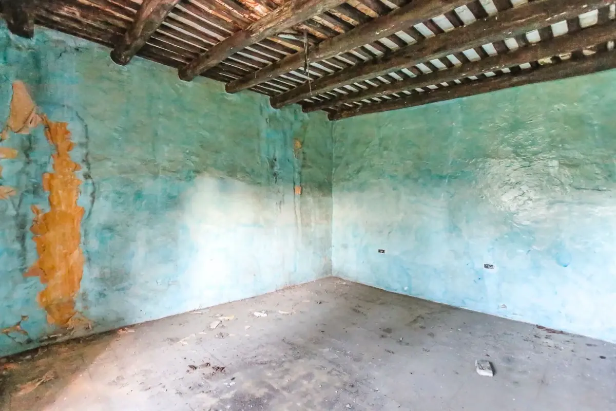 Interior de una masía antes de la reforma con paredes deterioradas y vigas de madera dañadas
