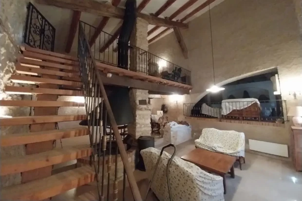 Interior reformado de una masía con vigas de madera, paredes de piedra y altillo